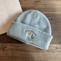 Dettaglio del berretto grigio a coste con ricamo a forma di cane su tavolo in legno - M (55-59cm) / Blu Chiaro