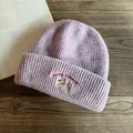 Dettaglio di un berretto in maglia viola con ricamo di cane carino su tavolo di legno - M (55-59cm) / Viola
