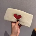 Detailed texture of off-white knitted headband with red heart patch in hands - Beige