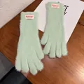 Detalle de guantes de felpa verde claro con etiqueta tejida sobre una mesa de madera - Talla única / Dedo Completo / Verde menta