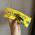 Detailed close-up of yellow knit headband with blue and white shooting star embroidery - Yellow