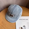 Detail of light blue denim camp cap with square logo patch and metal ring accent - Adjustable / Light Blue
