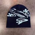 Dettaglio del berretto in maglia blu scuro con motivo a rana azzurra su una superficie ruvida - M (52-58cm) / Blu navy