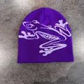 Dettaglio ravvicinato di un berretto viola in maglia con motivo jacquard a rana bianca - M (52-58cm) / Viola