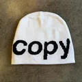 Close-up of white knit beanie with black woven letters on a dark textured background - M (54-59cm) / White