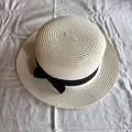 Dettaglio di un cappello di paglia a tesa piatta con nastro nero e fiocco elegante - Bianco