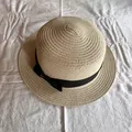Vista dall'alto di un cappello di paglia beige con fiocco nero su un tessuto bianco morbido - Beige