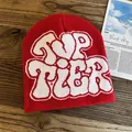 Detailed close-up of red knit beanie featuring white TOP TIER jacquard on wood surface - One Size / Red