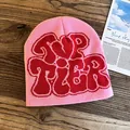 Detail of pink knitted beanie featuring red Top Tier jacquard lettering on wood texture - One Size / Rose Pink