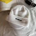 Gros plan d'un bonnet en tricot blanc avec broderie Studious noire et étiquette de marque - Blanc