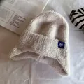 Dettaglio del berretto in maglia beige con toppa a fiocco di neve blu su fondo bianco - Taglia unica / Beige