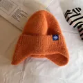Close-up of bright orange trapper hat showing fuzzy knit texture and snowflake patch - One Size / Orange