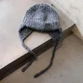 Detailaufnahme der grauen Strickmütze mit Ohrenklappen auf minimalistischem Beton - Einheitsgröße / Schwarz