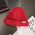 Detail of red ribbed knit beanie with small white NTRX label on a textured desk - M / Red