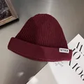 Close-up of wine red ribbed knit beanie featuring a white lettered fabric label - M / Burgundy