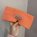 Detail of a bright coral orange knitted headband featuring a modern couture woven label - Orange