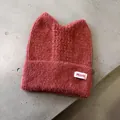 Detail der dunkelrosa Strickmütze mit süßen Katzenohren und gewebtem Textiletikett - Karamellbraun