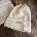 Détail d'un bonnet en maille épaisse blanc cassé avec écusson sur un fond en bois rustique - Taille unique (55-60cm) / Poche zippée