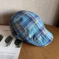 Détail d'une casquette plate à carreaux bleus et beiges sur une table en bois avec revue - M / Bleu lac