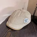 Detail of retro khaki flat cap featuring vintage embroidered shield badge and brown piping - M (55-59cm) / Beige