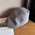 Detail view of a light gray flat cap on a wooden table next to a fashion magazine - One Size (55-58cm) / Gray