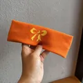 Detail eines orangefarbenen Strickstirnbands mit gelber Schleife und weicher Wollmischung - Orange