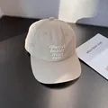 Close-up detail of white embroidery text on a beige cotton baseball cap surface - Adjustable / Beige