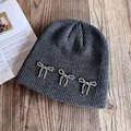 Detail of dark grey knit beanie featuring silver beaded bow accents on wooden background - M / Dark Heather Grey