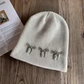 Detail of cream knit beanie with silver beaded bows on textured dark wood background - M / Beige
