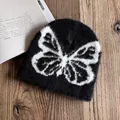Detailaufnahme der schwarzen Strickmütze mit weißem Schmetterling auf Holzoberfläche - M (54-58cm) / Schwarz