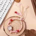 Detail of pink hand-woven rope watch with rhinestone dial and tassel on wood base - White