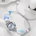 Detail einer quadratischen Quarzuhr mit Perlenarmband auf einem Keramiktablett - Hellblau