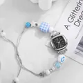 Detail einer quadratischen silbernen Uhr mit gewebtem Armband und dekorativen blauen Perlen - Schwarz