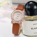 Detail of luxury rose gold ladies watch with crystal bezel leaning on a perfume bottle - Tan