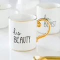 Close-up of ceramic mugs with gold handles and 'his BEAUTY' 'her BEAST' artistic text - Beauty Pattern / Beauty