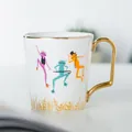 Tazza in ceramica bianca con rane colorate, manico dorato e base elegante - Stile Rana