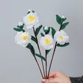 Handmade white crochet camellia bouquet with green leaves held against a grey background - White