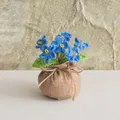 Detailansicht handgefertigter blauer Häkelblumen im braunen Leinensack-Übertopf - 6-Kopf blaues Vergissmeinnicht-Stil