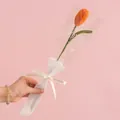Handmade knitted orange tulip in elegant gift wrap with a white love ribbon on pink background - Tulip Orange