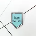 Close-up of Team Awesome enamel shield pin with light blue finish and arrow detail - Light Blue Shield (XZ0756) / Light Blue (XZ0756)