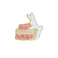 Enamel pin detail of a white bunny on a pink cream cake with gold heart accents - C1755