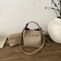 Secchiello kaki con trama litchi, chiusura dorata e foulard decorativo su tavolo in legno - Cachi