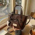 Sac seau marron foncé verni avec nœud et breloque ours posé sur une table en bois - café