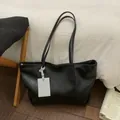 Minimalistische schwarze Kunstleder-Tragetasche mit weißem Anhänger in gemütlicher Szene - Schwarz