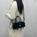 Sac Boston en cuir noir avec détails dorés porté en bandoulière sur un manteau beige - Noir