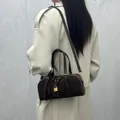 Sac Boston en cuir marron foncé avec cadenas doré porté sur un trench-coat beige - café