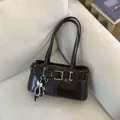 Minimalistische dunkelbraune Schultertasche mit Perlenbogen-Anhänger auf Sofa - Mit Anhänger / Braun