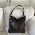 Dark brown oil-wax leather tote bag with silver eyelets on a white sofa - Coffee - No Pendant