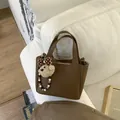 Brown litchi grain bucket bag with a plush bear charm and white beaded lanyard accessory - With Pendant / Brown