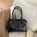 Borsa tote minimalista in ecopelle nera con fibbia argentata su un divano bianco - senza ciondolo / Nero